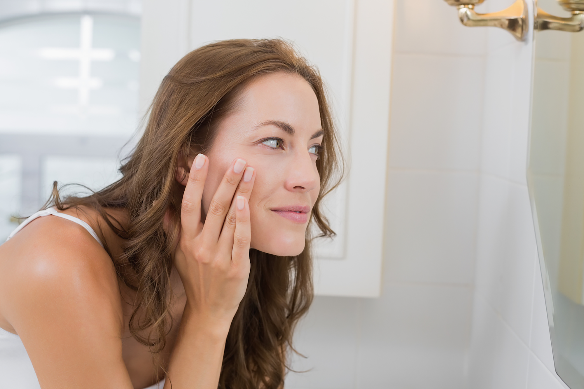 Side view of a beautiful young woman examining her face in the bathroom at home
